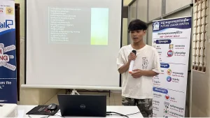 Hou Heng presenting beside a laptop and projected presentation in an FLC classroom.
