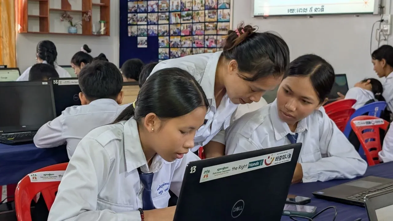 Three students in school uniforms work together on a laptop during an ICT training session in a computer classroom.