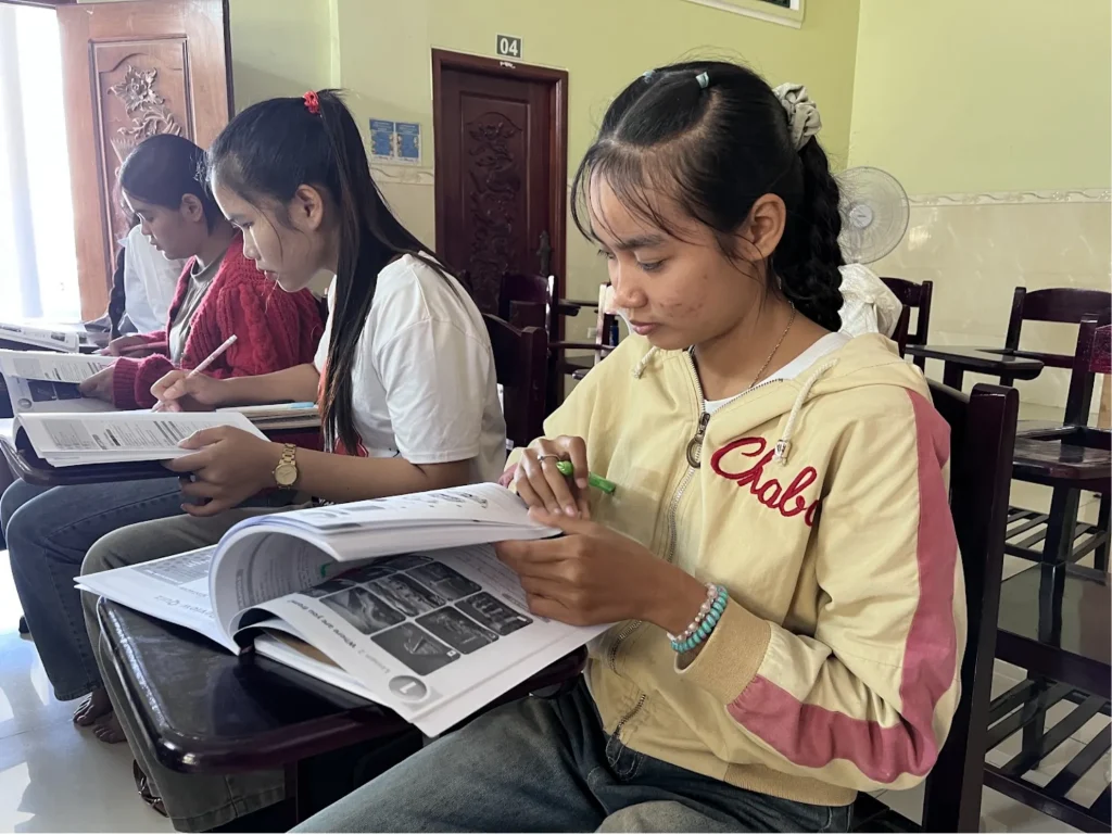 neang sounanita Neang Sounanita reading an open learning booklet while seated with classmates.