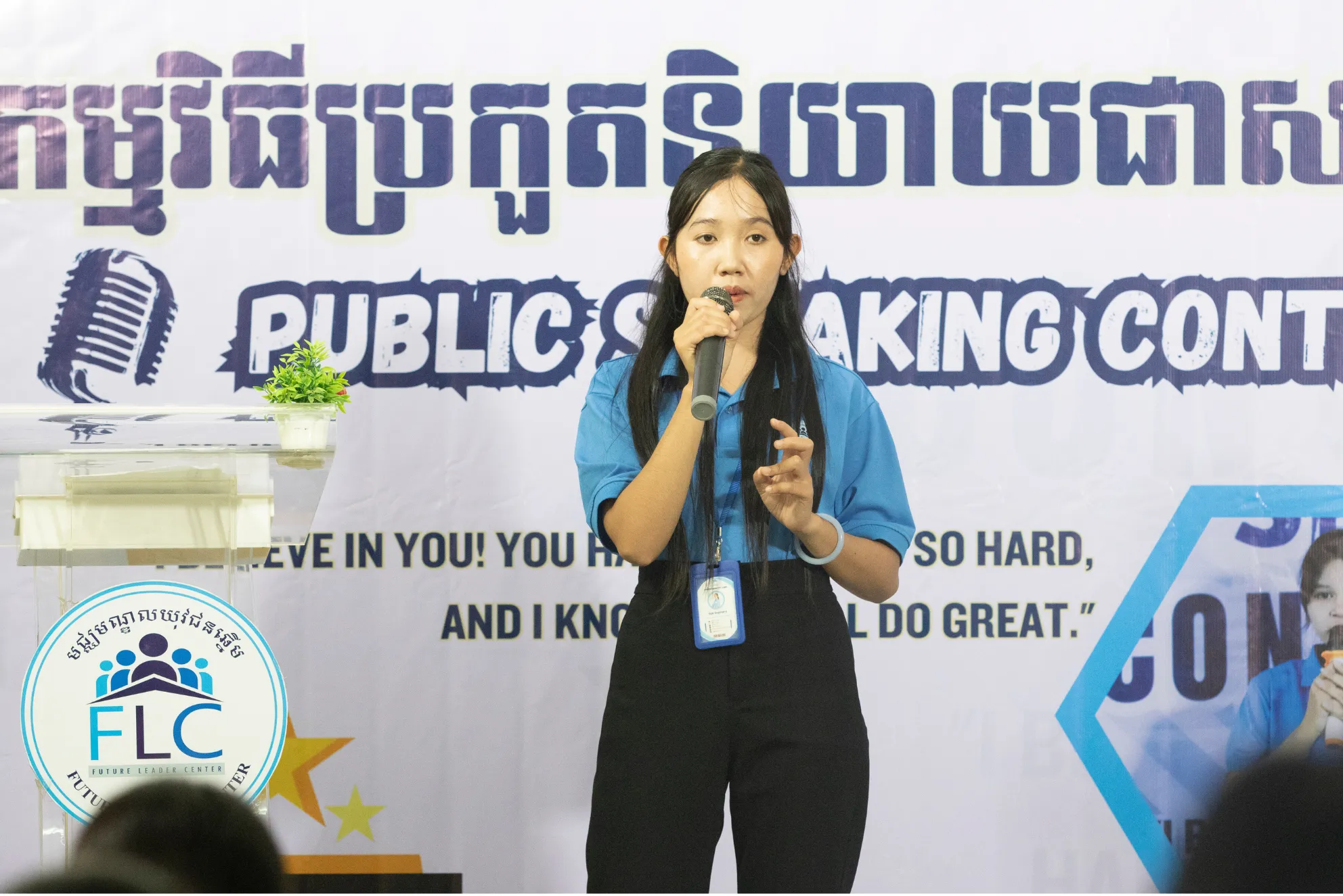Sok Sophary speaking into a microphone and gesturing during an FLC public speaking contest.